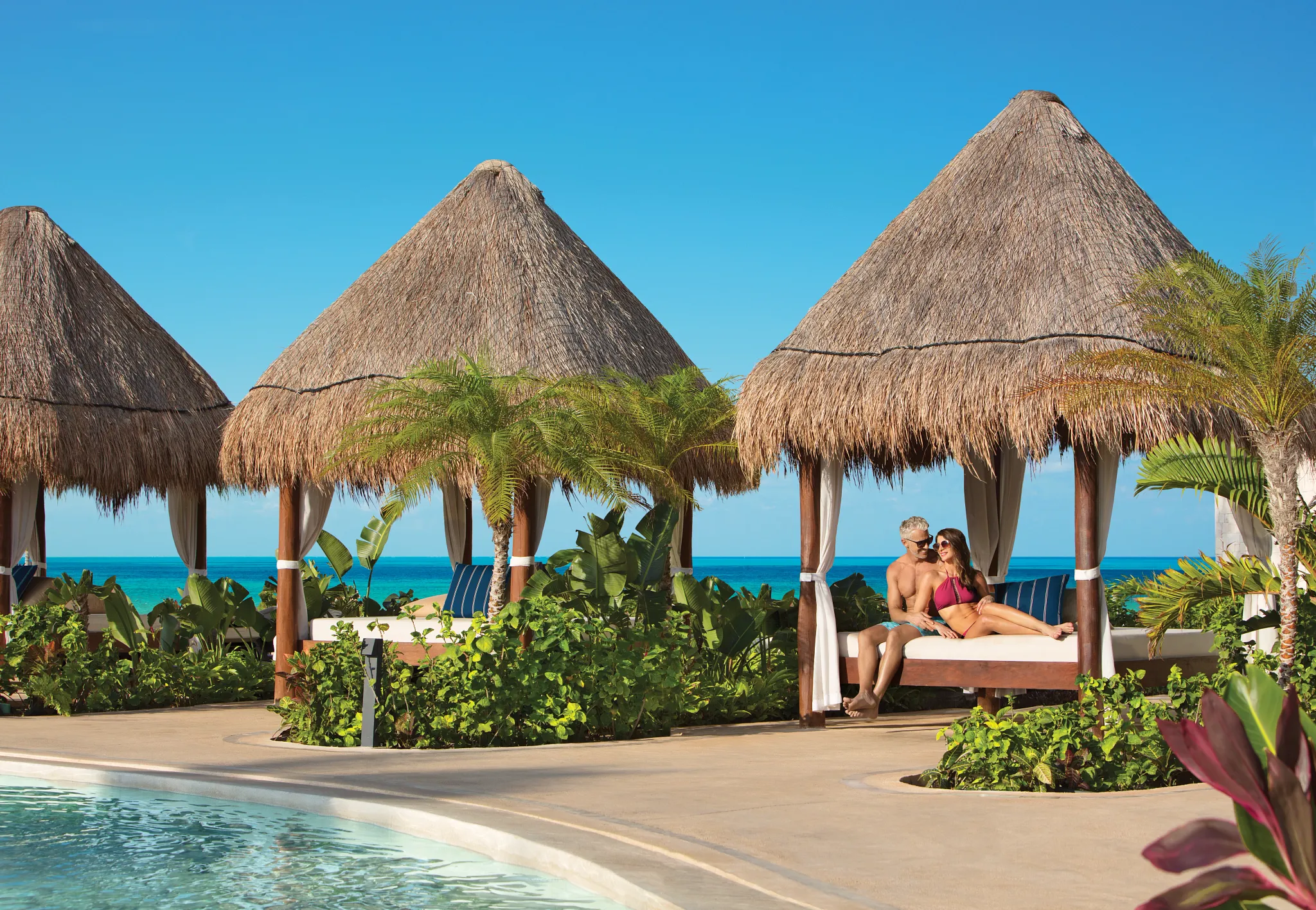 Couple relaxing in a private Balinese bed cabana near the pool at Dreams Playa Mujeres Resort.