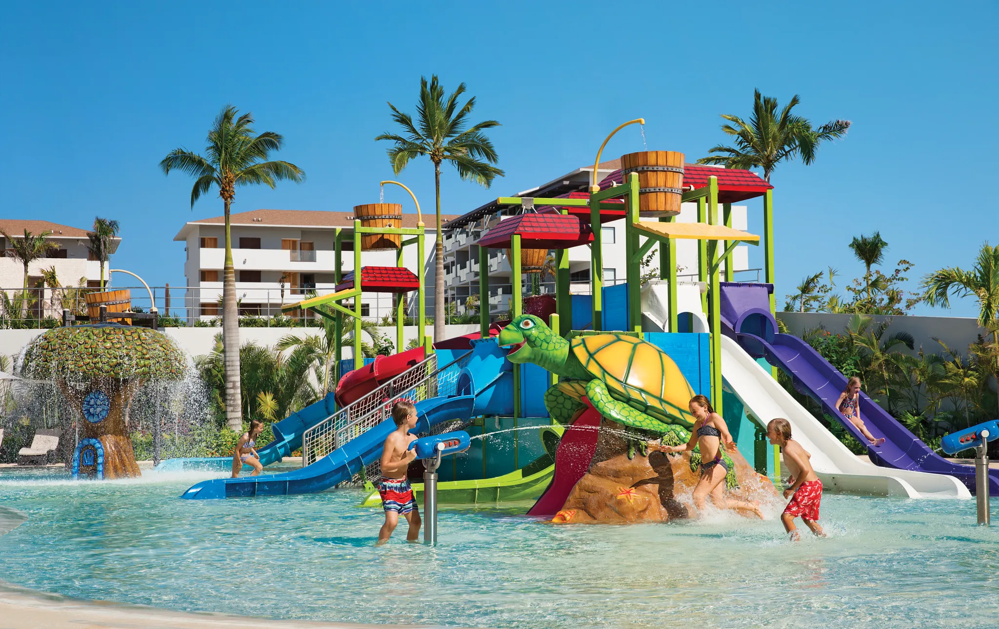 Kids playing in a colorful water park with slides at Dreams Playa Mujeres Resort.