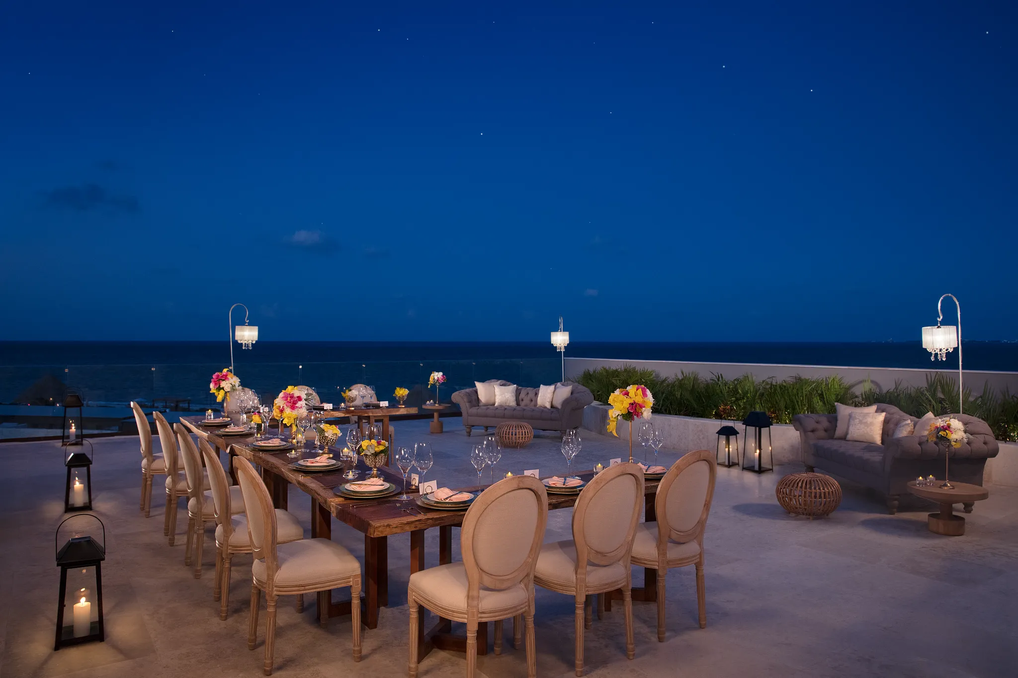 Outdoor terrace set for dinner with ocean view at night.