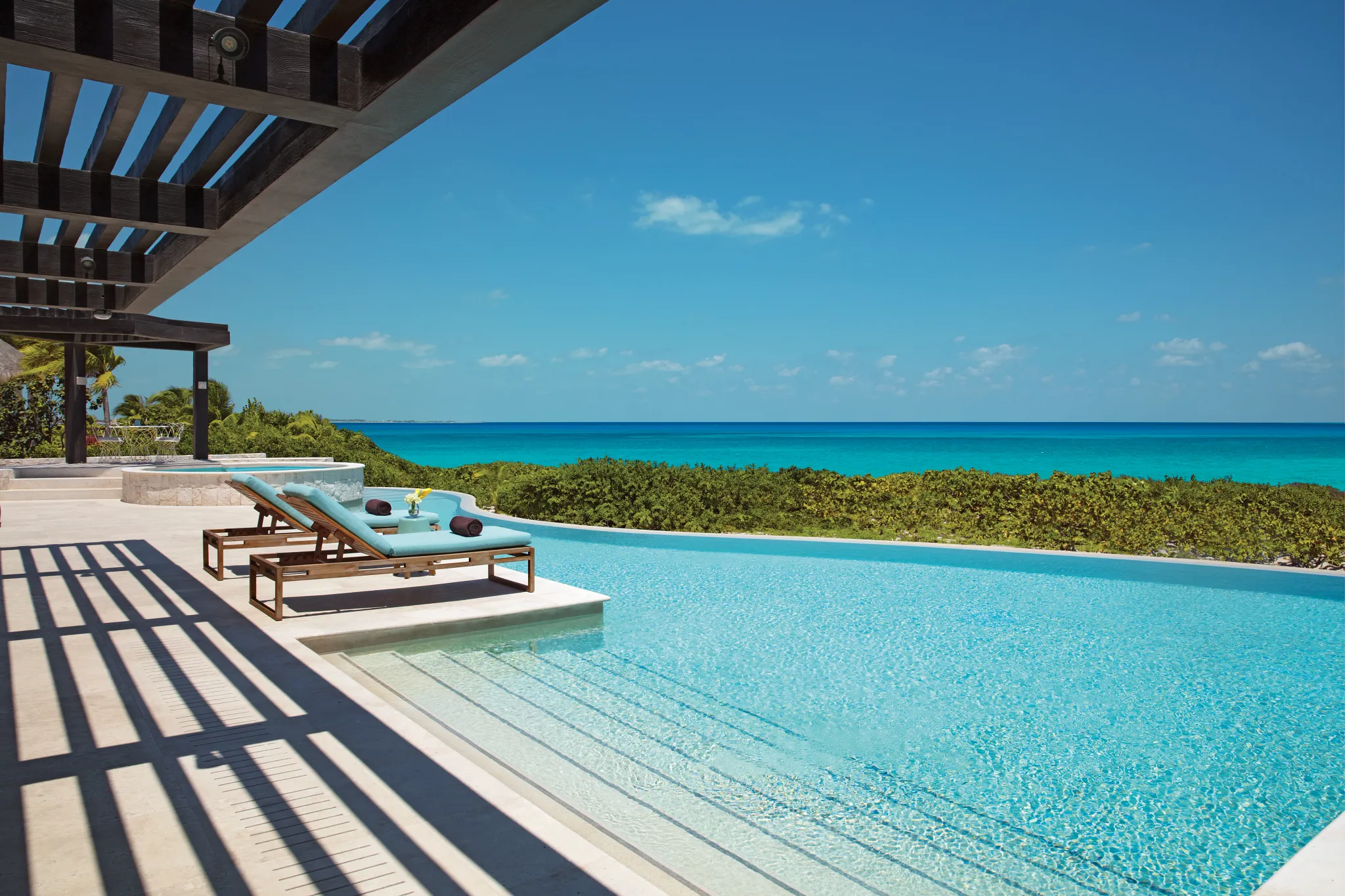 Private infinity pool overlooking the ocean with lounge chairs.